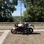 Moto sportiva parcheggiata con casco su un belvedere alberato, con vista panoramica sullo sfondo