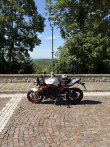 Moto sportiva parcheggiata con casco su un belvedere alberato, con vista panoramica sullo sfondo