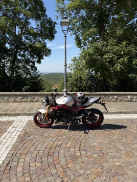 Moto sportiva parcheggiata con casco su un belvedere alberato, con vista panoramica sullo sfondo