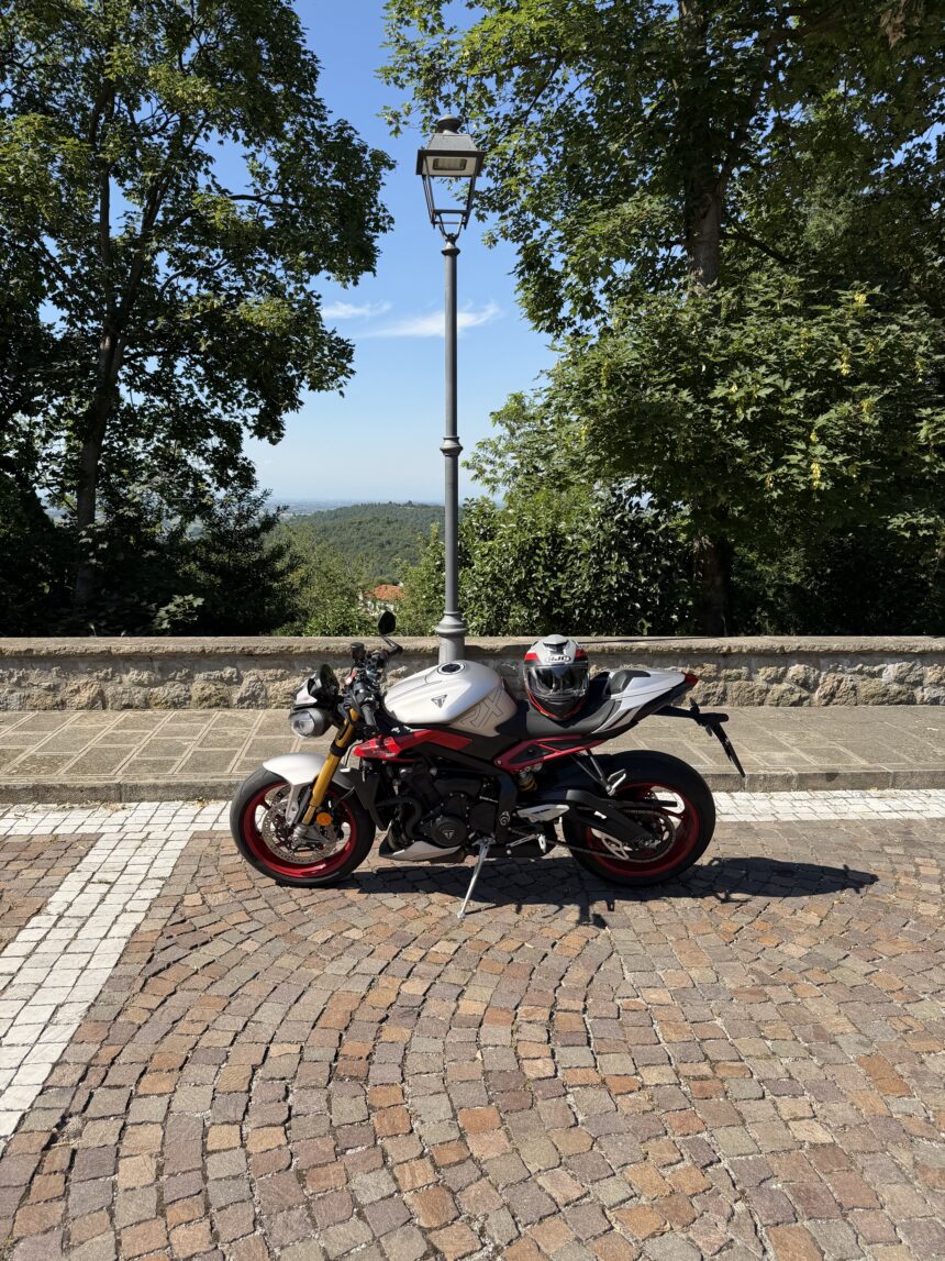 Moto sportiva parcheggiata con casco su un belvedere alberato, con vista panoramica sullo sfondo